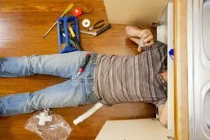person laying on back fixing kitchen sink pipes