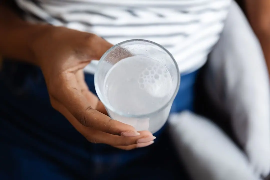Side view of young African American woman holding a glass of cloudy tap water with a dissolving pill, showing self-care for illness. Healthcare and medicine concept