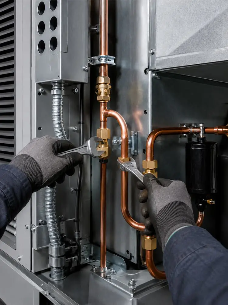 Close-up of a commercial HVAC installation in Fort Mohave AZ, with gloved hands using wrenches on copper piping and brass fittings.