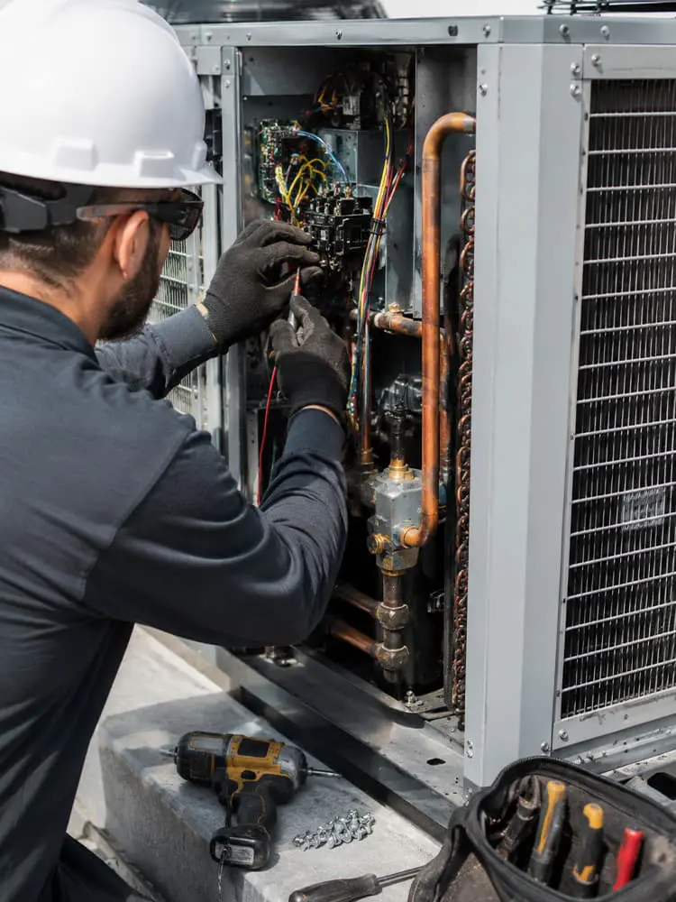 HVAC technician working on a commercial air conditioning installation in Golden Valley AZ, inspecting wiring and internal components of a rooftop AC unit.