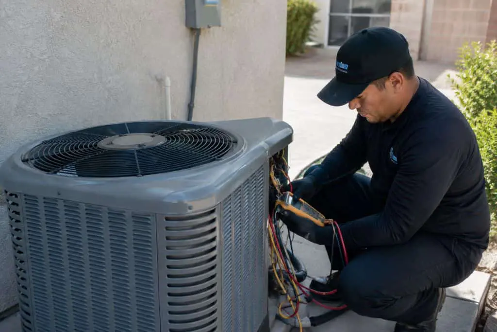 HVAC technician testing electrical components inside a residential outdoor AC condenser