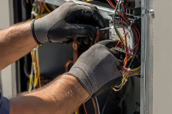 Close-up of an HVAC technician wiring a commercial air conditioning unit.