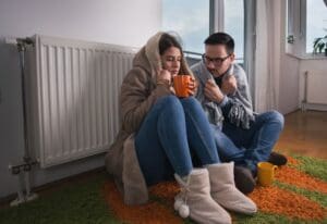 A cold couple huddles near a broken heater.
