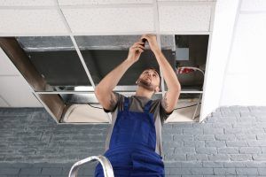 repair technician fixes air conditioning unit in ceiling