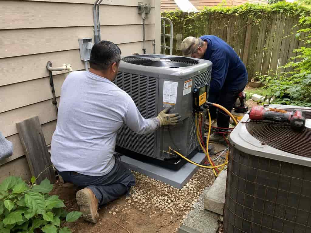 Two HVAC technicians installing and connecting a residential outdoor air conditioning unit